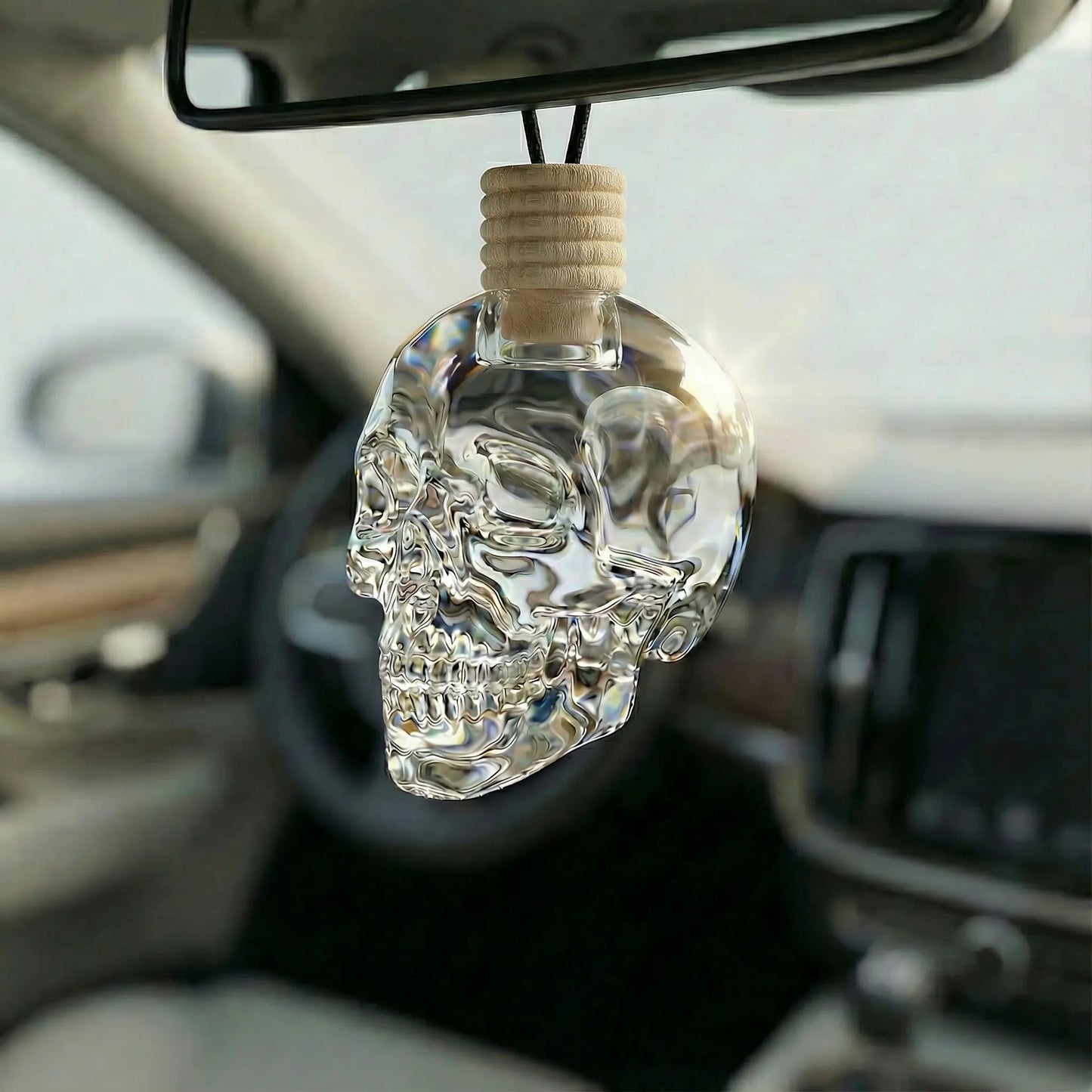 8ml Glass Skull bottle hanging from a rear view mirror in a car. There is liquid in the bottle .