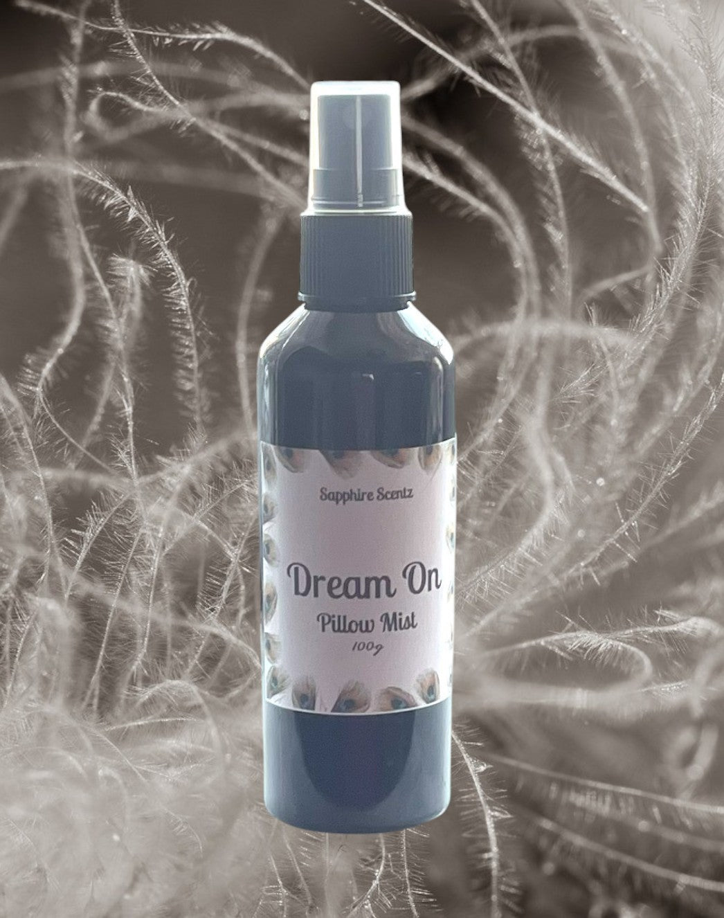 A spray bottle labeled 'Dream On Pillow Mist' with a grey cap, surrounded by a decorative background that includes plants and mist.