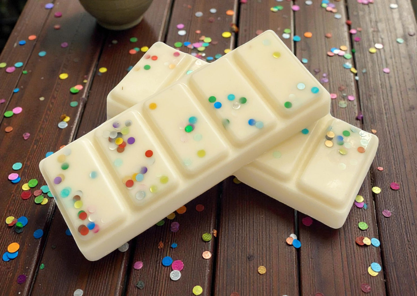 White chocolate bars with colorful sprinkles on a wooden surface with confetti.