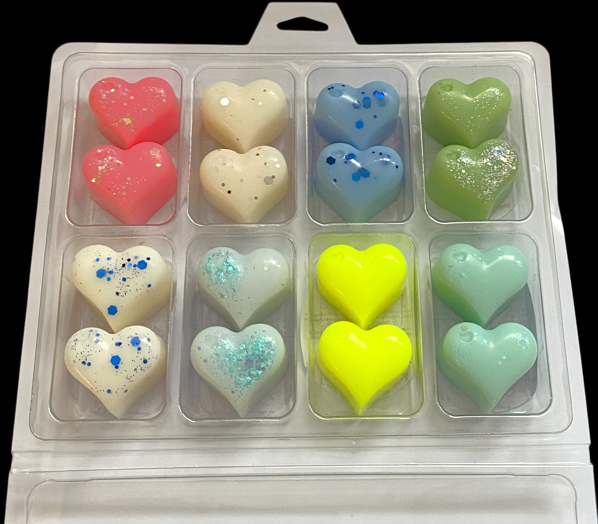 A collection of heart-shaped wax tarts in various colors including pink, white, blue, turquoise, yellow, and green, packaged in a clear plastic box.