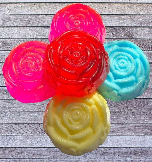 A selection of rose-shaped soap bars in different colors including pink, red, blue, and yellow, arranged on a wooden surface.