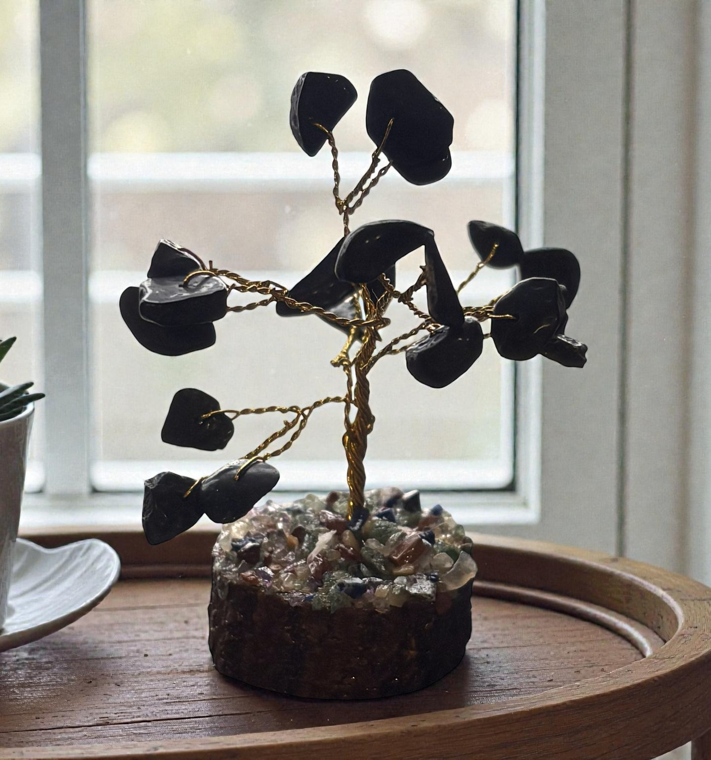 Decorative tree made of black stones on a wooden surface with a blurred window background