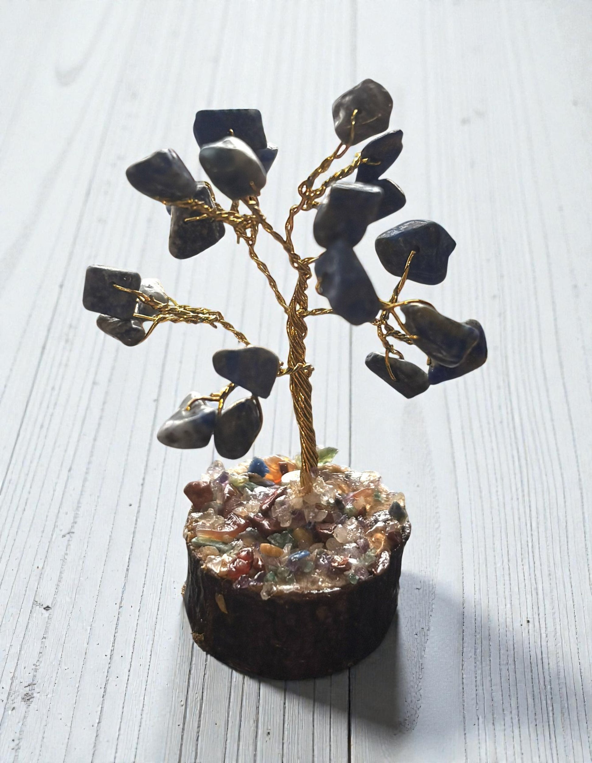 Decorative tree made of black stones and gold wire on a white wooden surface