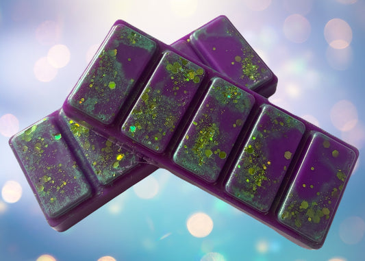 A snap bar wax with sections of purple wax containing green speckles, displayed against a blue bokeh background.