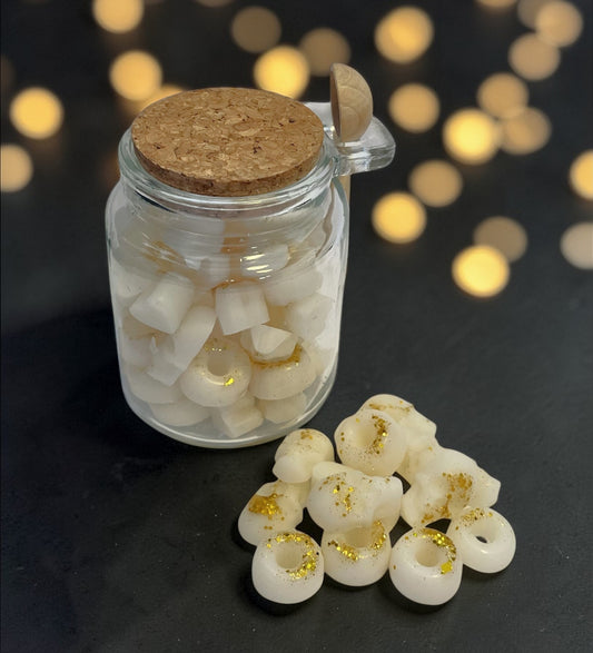 Jar of white donut-shaped candies with gold glitter on a dark surface with blurred lights in the background