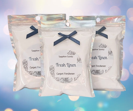 Three packets of 'Fresh Linen' carpet freshener with a blue ribbon on each, set against a bokeh background.