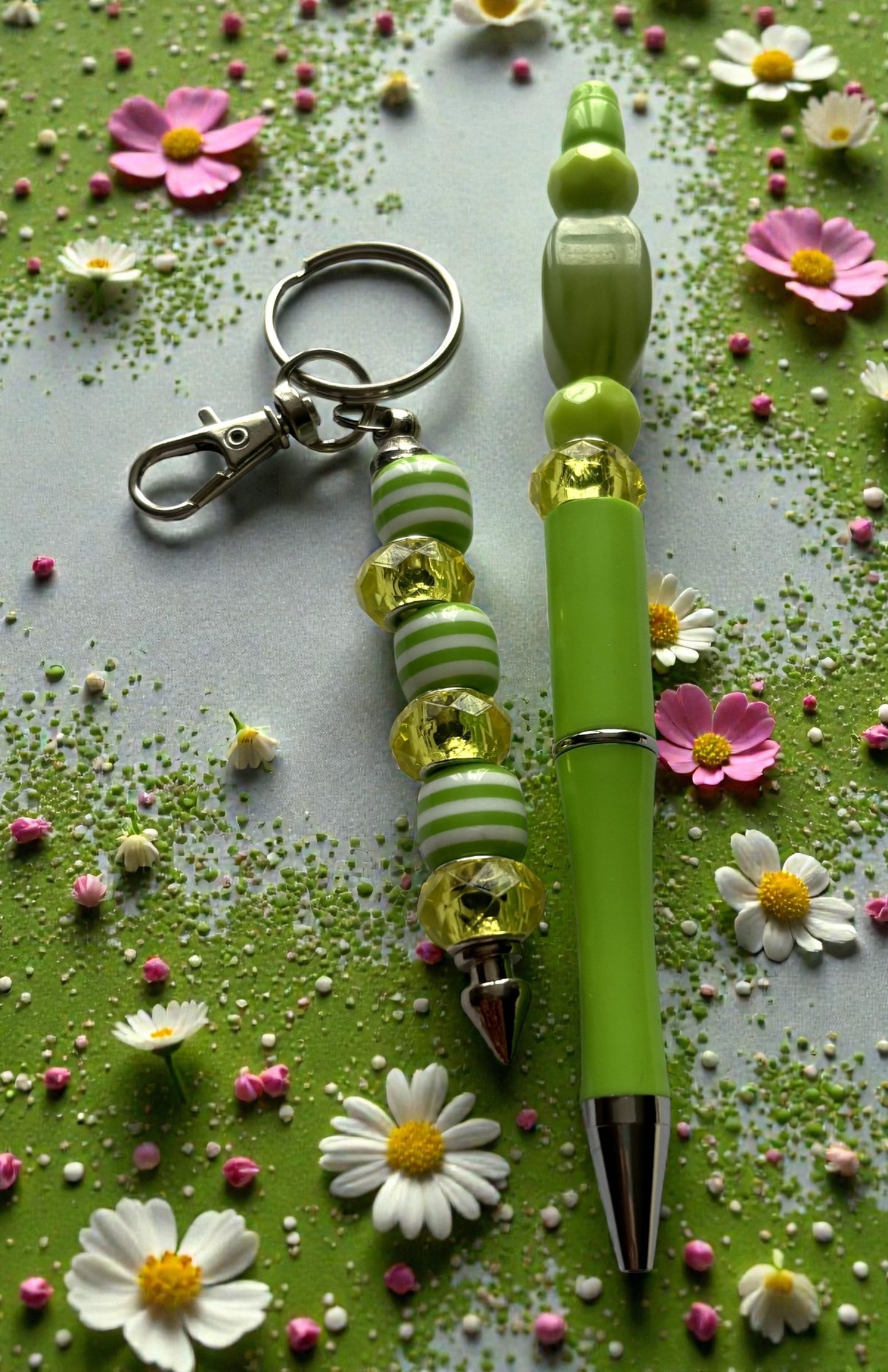Green pen with decorative beads and keychain on a green background with flowers