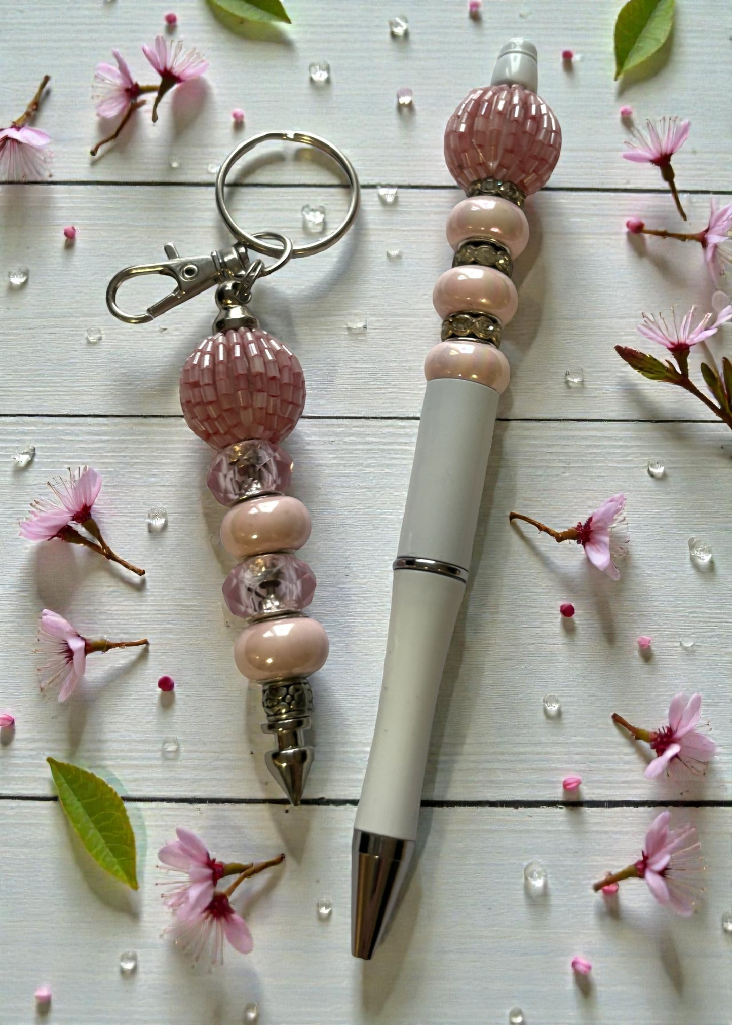 Pen with decorative bead holder and keychain on a wooden surface with cherry blossoms.