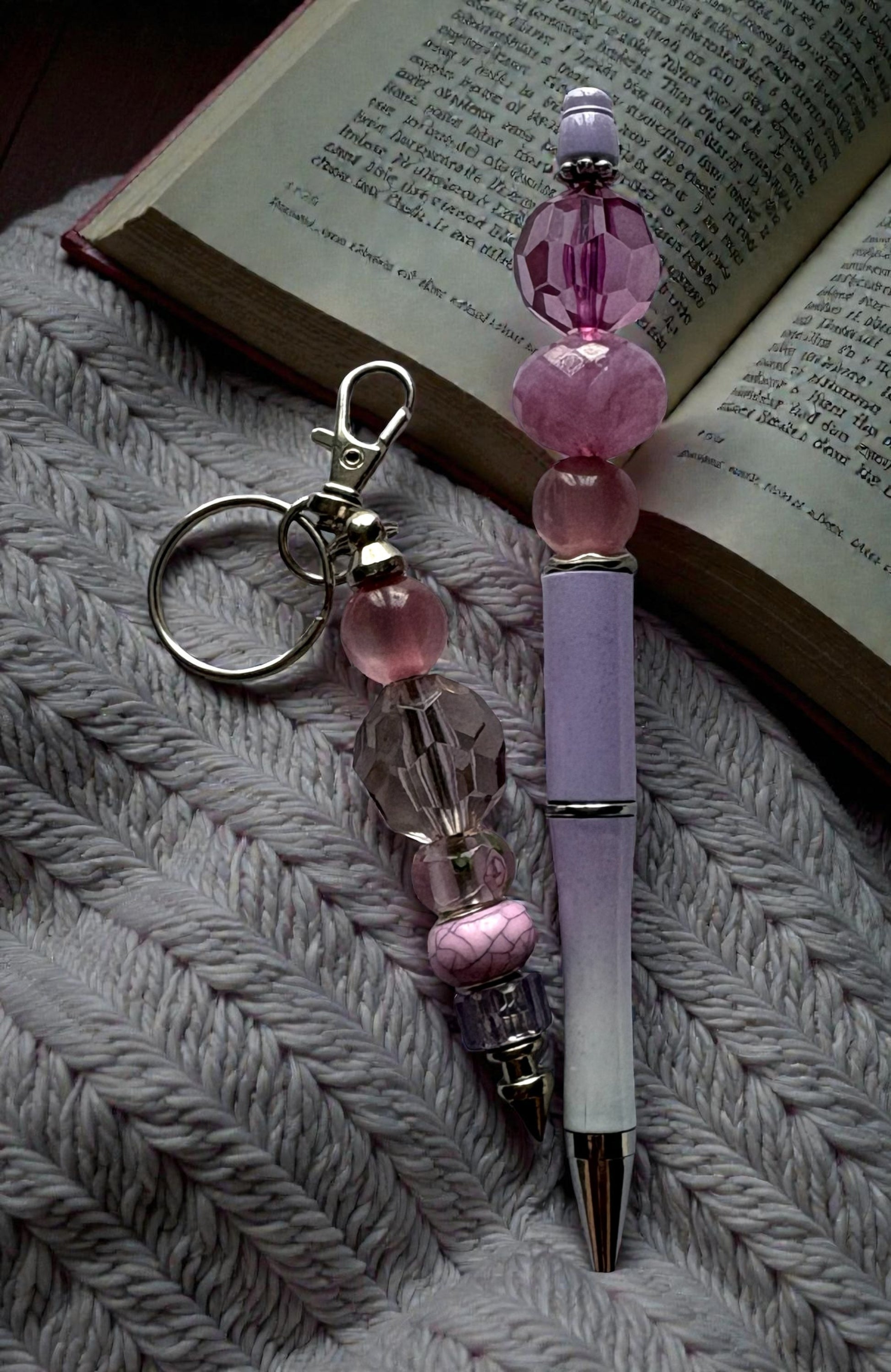 Pink beaded keychain and pen on a textured surface with an open book in the background