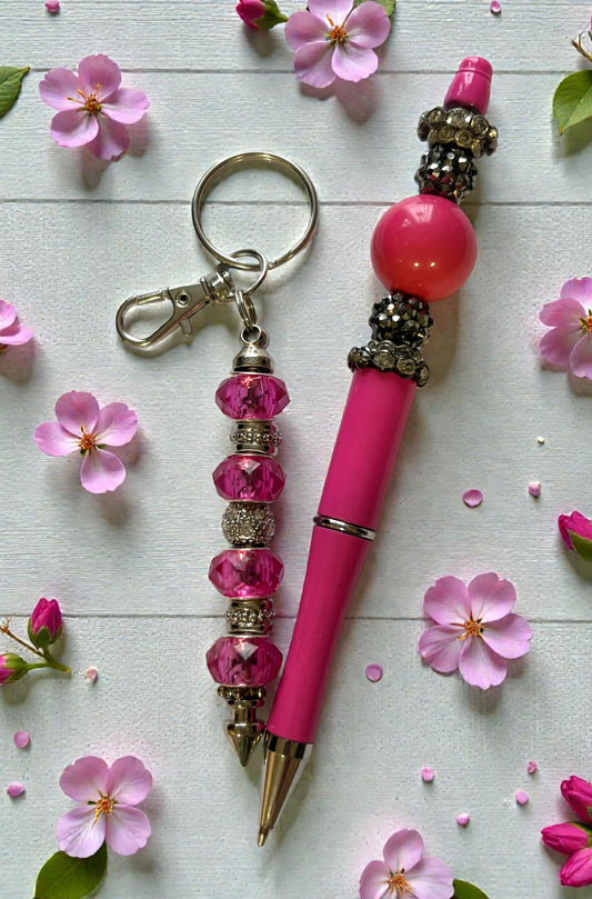 Pink pen and keychain with decorative beads on a light surface with pink flowers.
