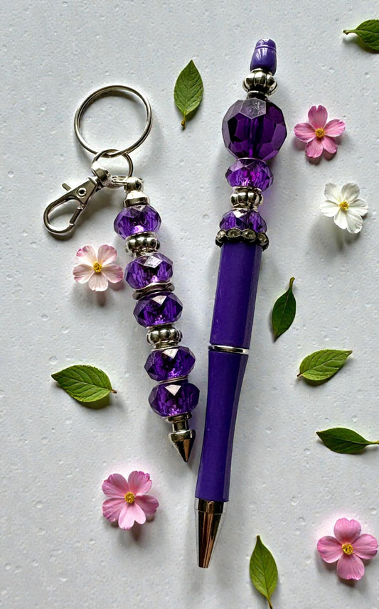 Purple beaded keychain and pen with decorative flowers and leaves on a light gray background