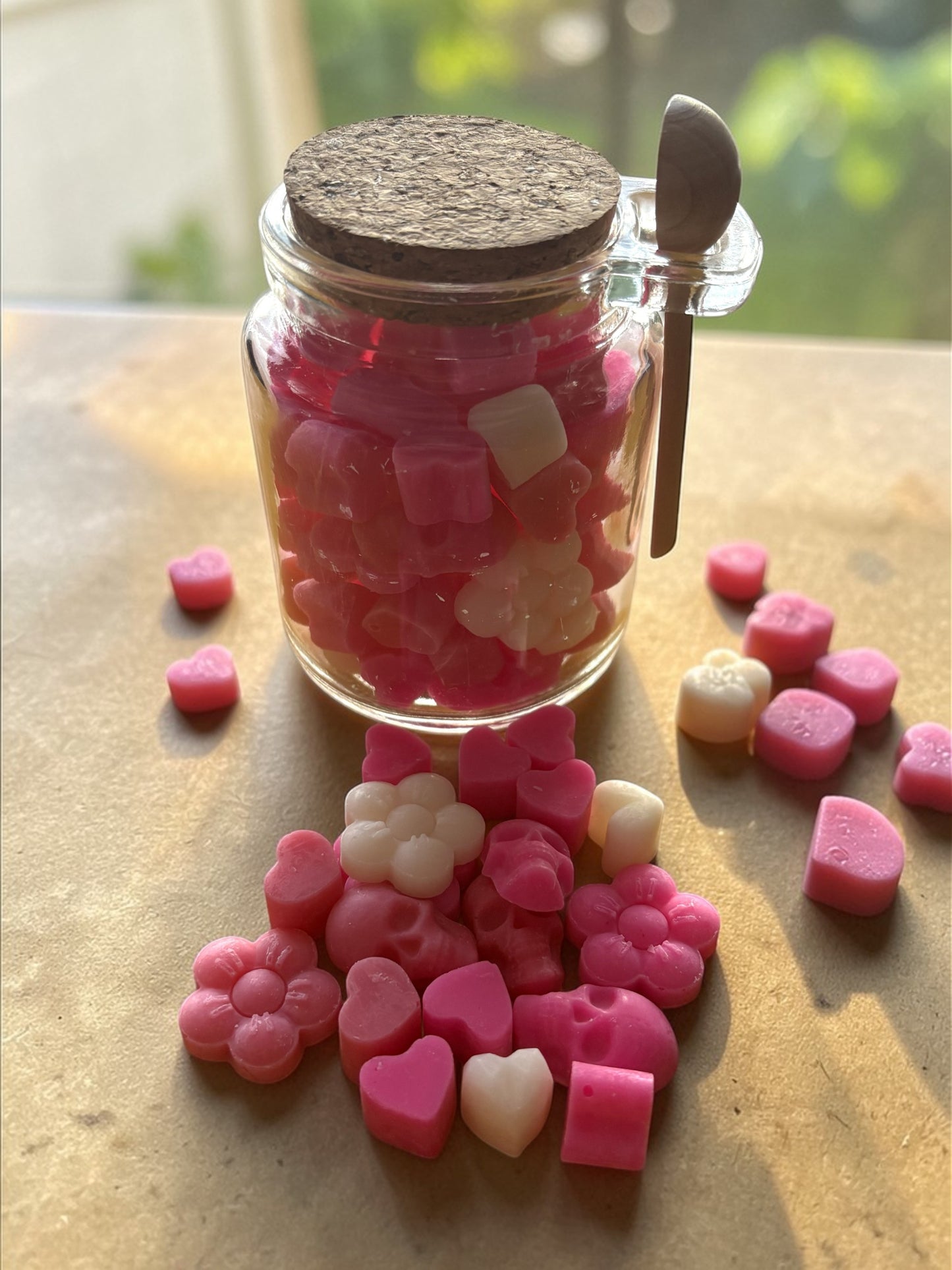 Jar of pink and white heart-shaped candies with a cork lid on a wooden surface.