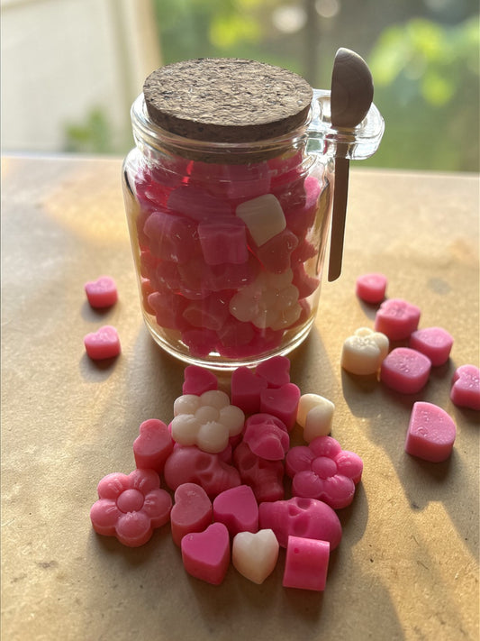 Jar of pink and white heart-shaped candies with a cork lid on a wooden surface.