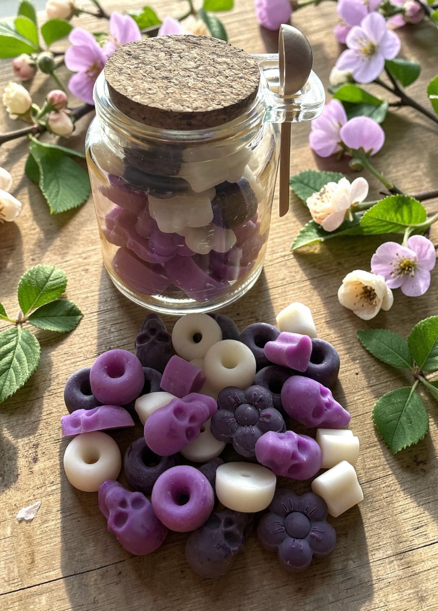 Jar of decorative beads with a wooden lid on a wooden surface with flowers and leaves.
