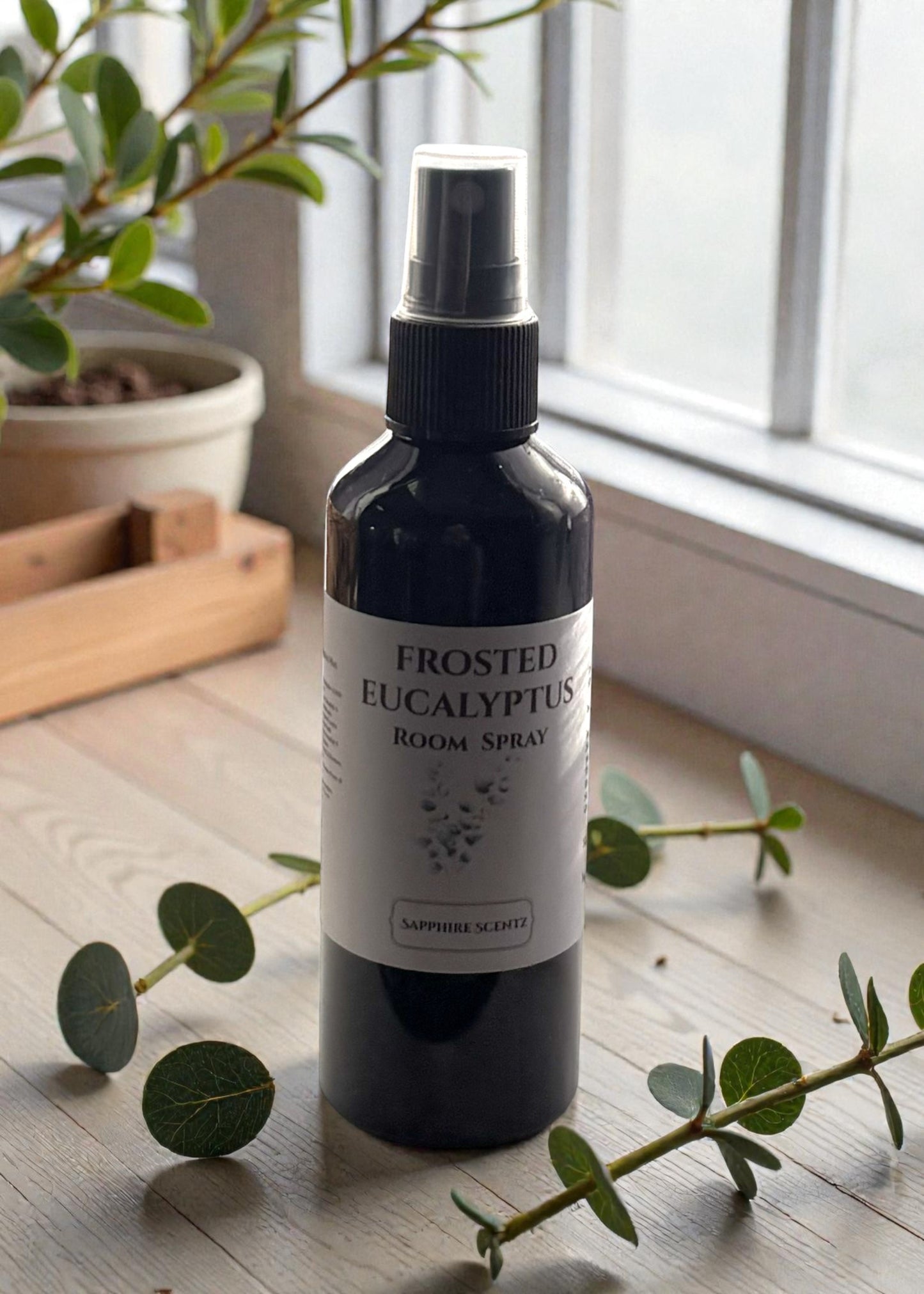 Frosted Eucalyptus room spray bottle on a wooden surface with eucalyptus leaves.