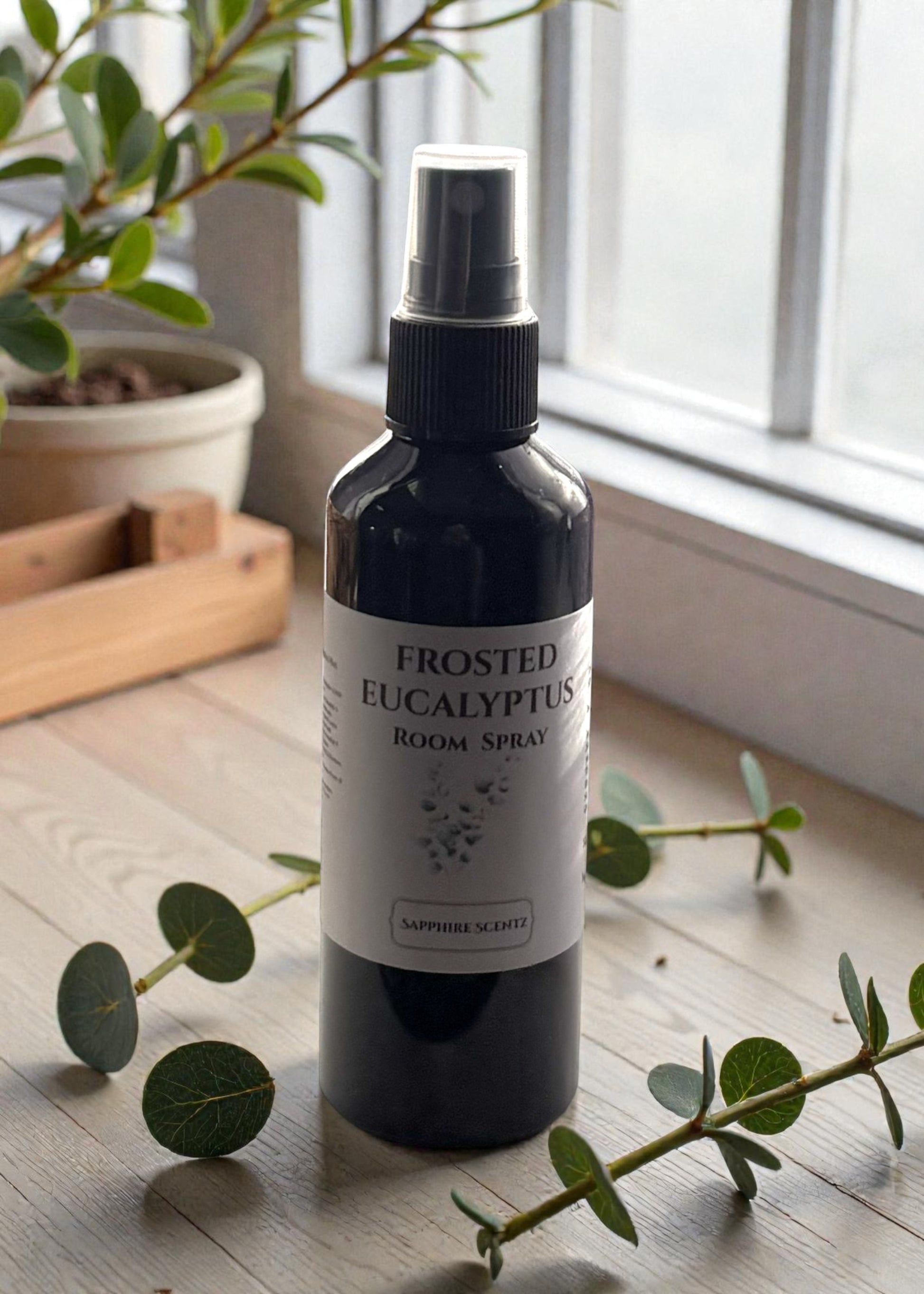 Frosted Eucalyptus room spray bottle on a wooden surface with eucalyptus leaves.