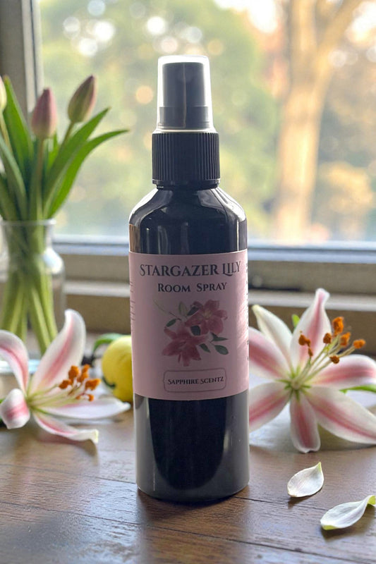 Room spray bottle labeled 'Stargazer Lily' on a wooden surface with flowers in the background.