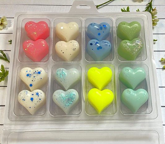 Heart-shaped bath bombs in various colors in a clear plastic packaging on a wooden surface.