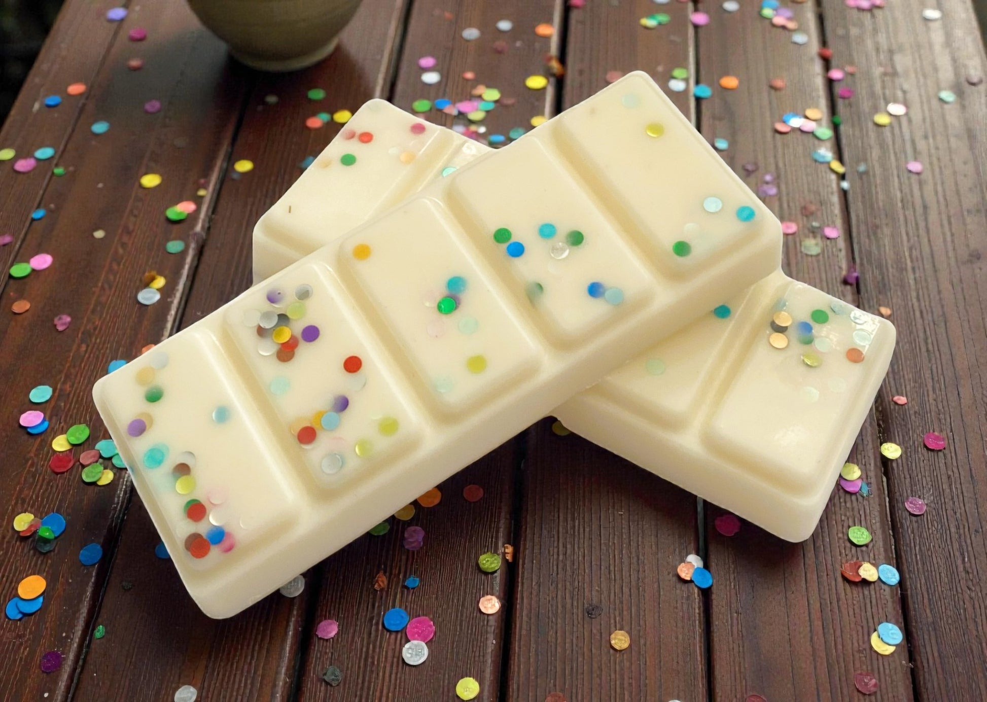 White chocolate bars with colorful sprinkles on a wooden surface with confetti.