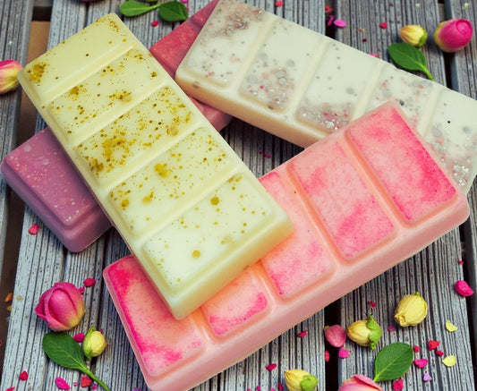 Assorted colorful soap bars on a wooden surface with flowers and leaves.
