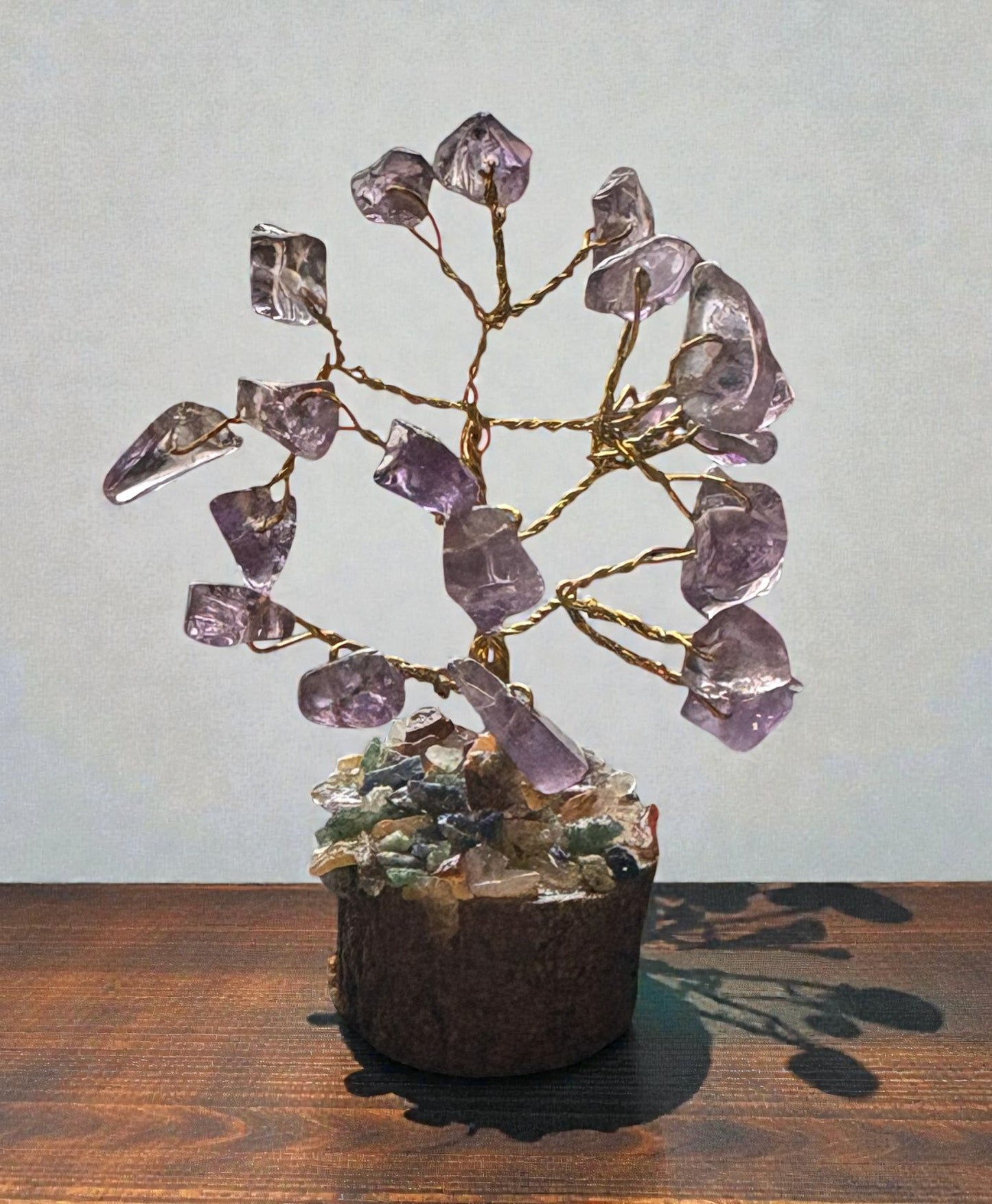Crystal tree with purple crystals on a wooden surface against a light gray background
