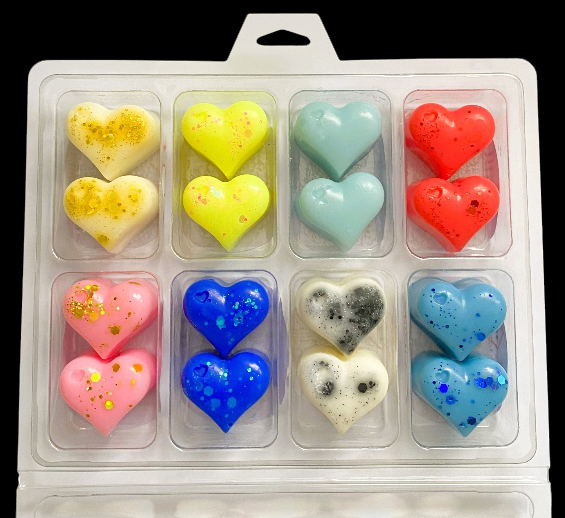 A clear plastic box containing multiple heart-shaped wax melts in various colors including yellow, red, blue, pink, and white, each with a different fragrance.